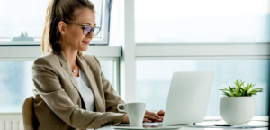 woman with glasses sitting at table and typing at a computer